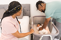 A mother and father preparing a crib for baby to sleep in.